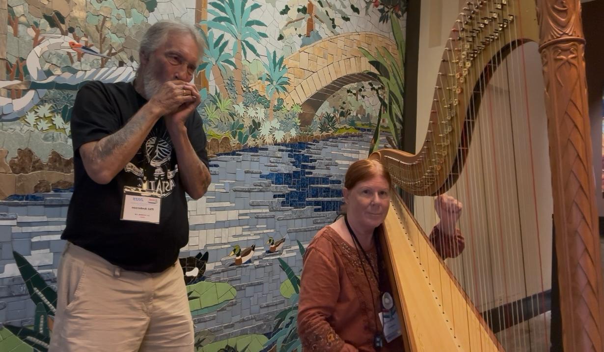 Phil on harmonica and Renee on concert harp performing before a mural